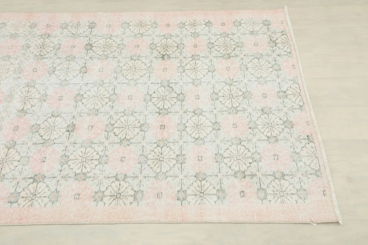 Close-up angled view of one corner of the rug, showing the faded rose field and geometric motifs
