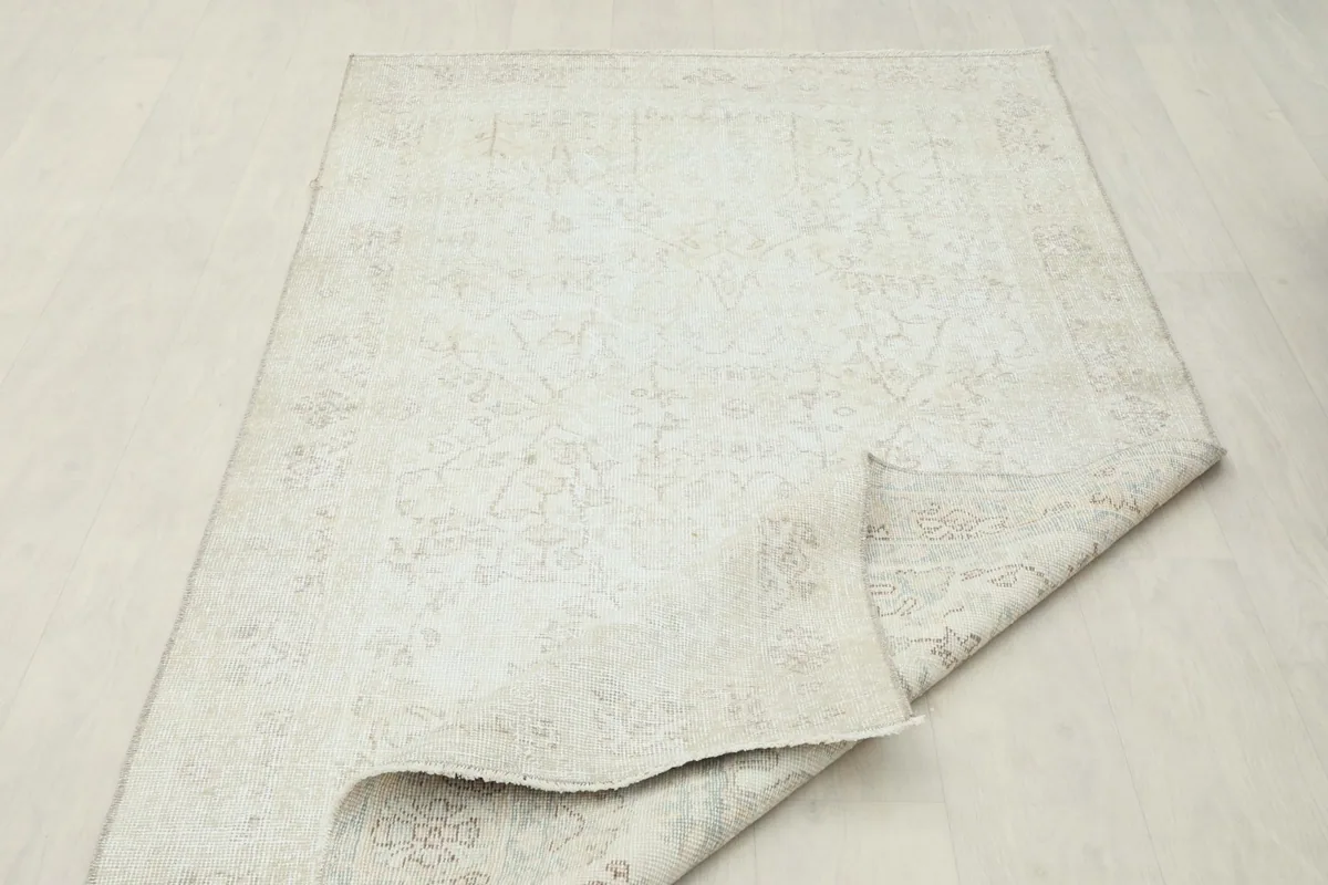 The ivory vintage rug partially folded, showing the flexibility and thickness of the material