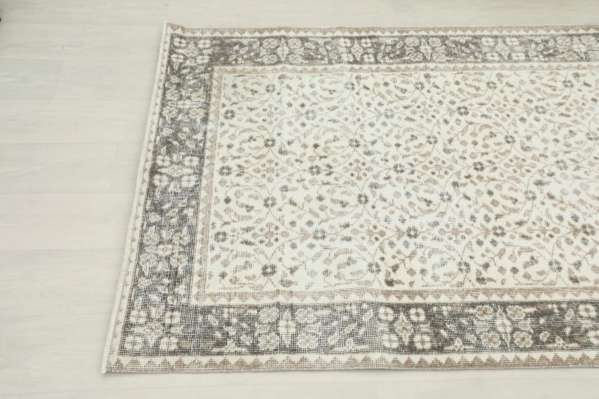 Angled close-up showing the intricate floral motifs in the ivory field and the darker gray border design.