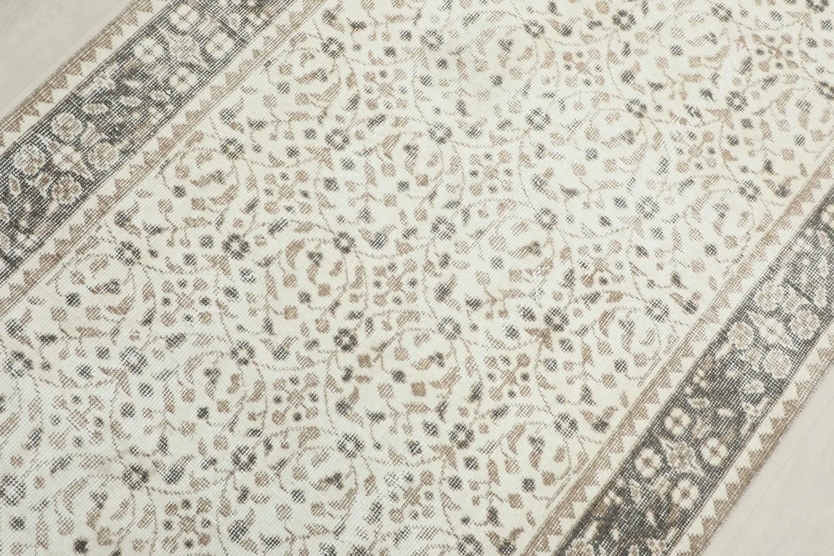 Overhead close-up of the rug's central field, revealing the delicate tan and gray floral patterns on ivory.