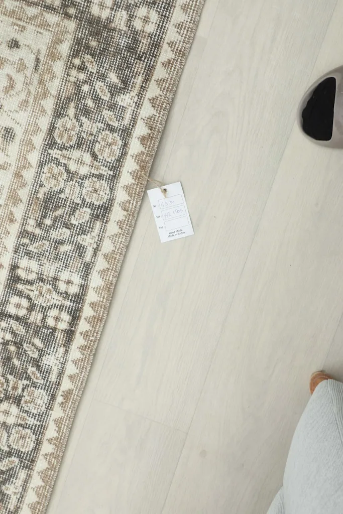 Close-up of a care tag on the floor next to the rug, with a person's foot nearby for scale.