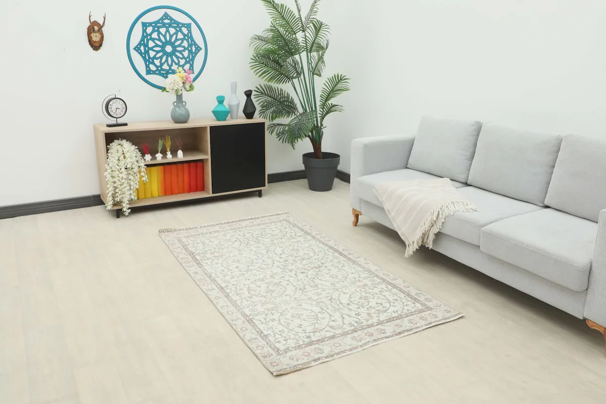Ivory vintage rug placed in a modern living room setting with a gray sofa and wooden cabinet