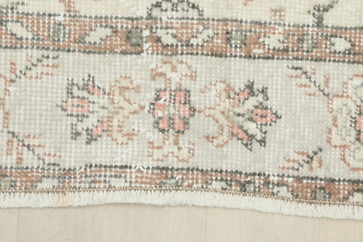 Detailed shot of the rug's border design with small floral elements and fringe