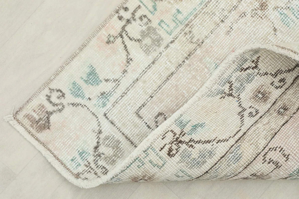 Corner of the rug folded back, revealing the reverse side and the cotton foundation.