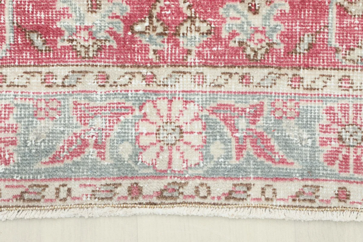 Close-up of the detailed geometric and floral border design in gray, rose, and beige colors.