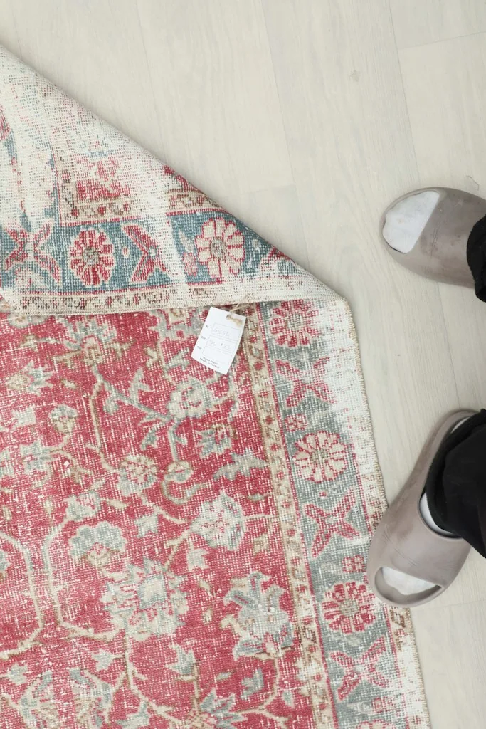 View of the back of the hand-knotted rug and its fringes, with feet in slippers for scale.