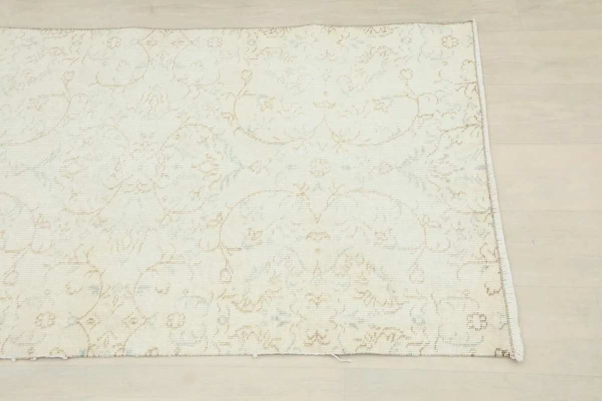 Close-up of one end of the cream runner, highlighting the faded floral motifs.