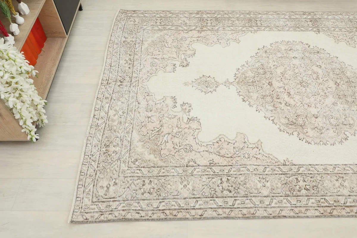 Corner view of the rug, showing the blend of ivory field and faded beige and gray medallion design.