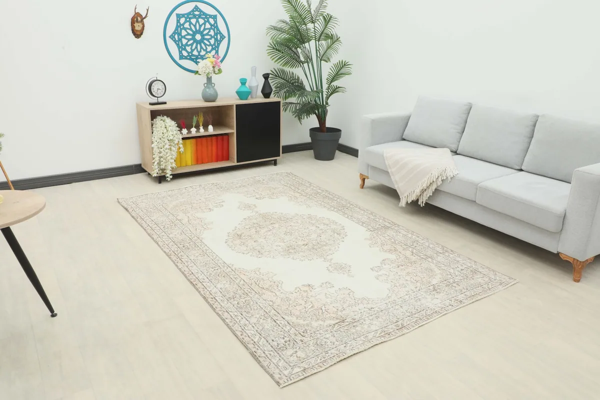 Vintage ivory and beige area rug placed in a modern living room setting with a light gray sofa and wooden cabinet.