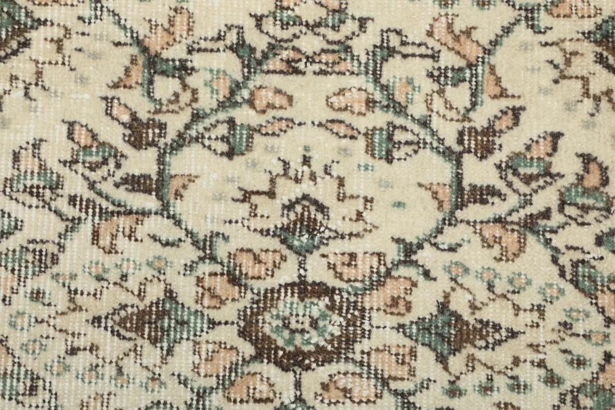 Macro detail of the hand-knotted floral patterns in ivory, brown, and green