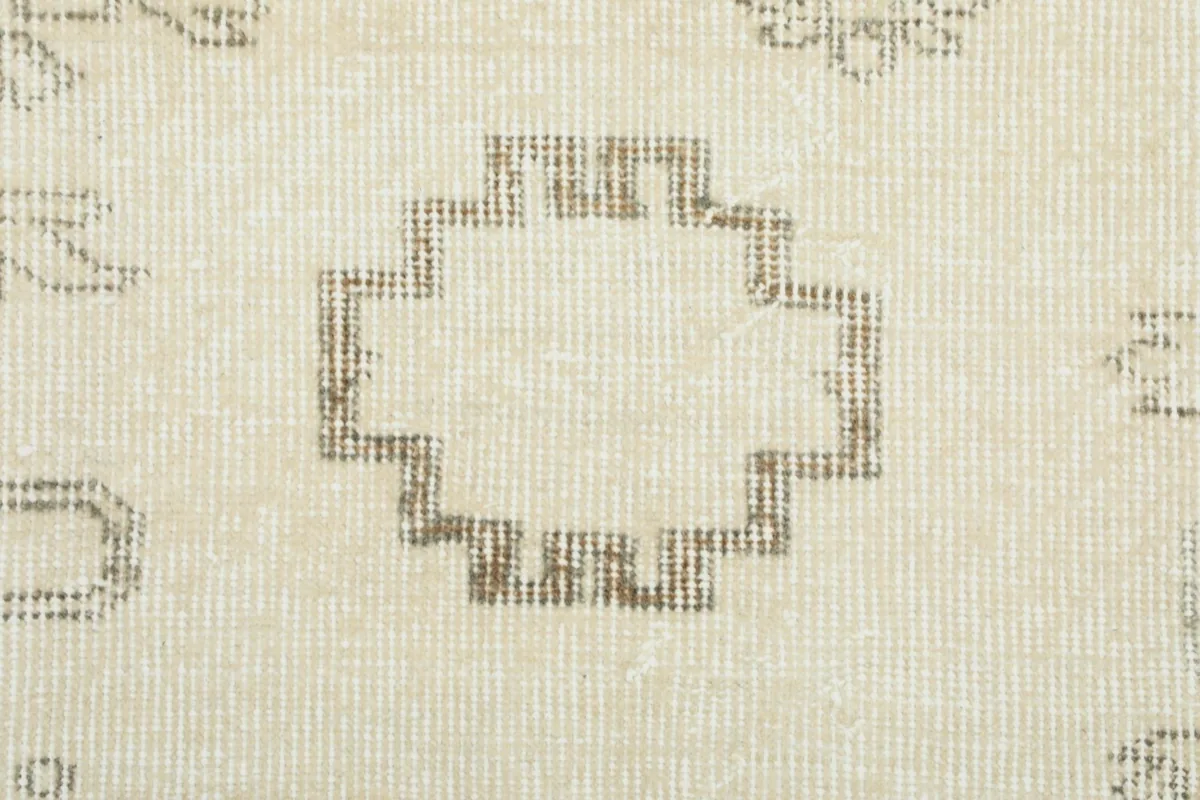 Macro close-up of a distinct geometric motif in faded tan and gray tones on the rug's ivory field.