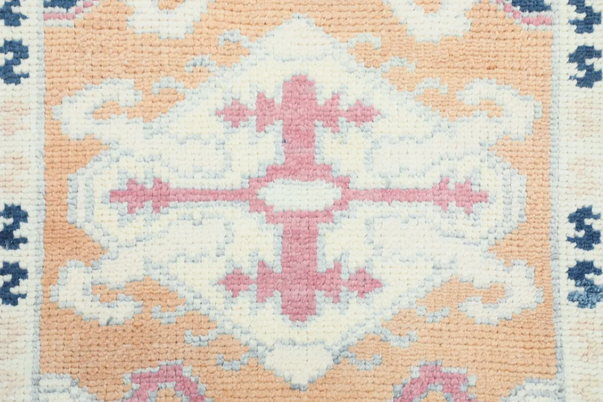 Extreme close-up of a pink and ivory geometric motif within the rug's design