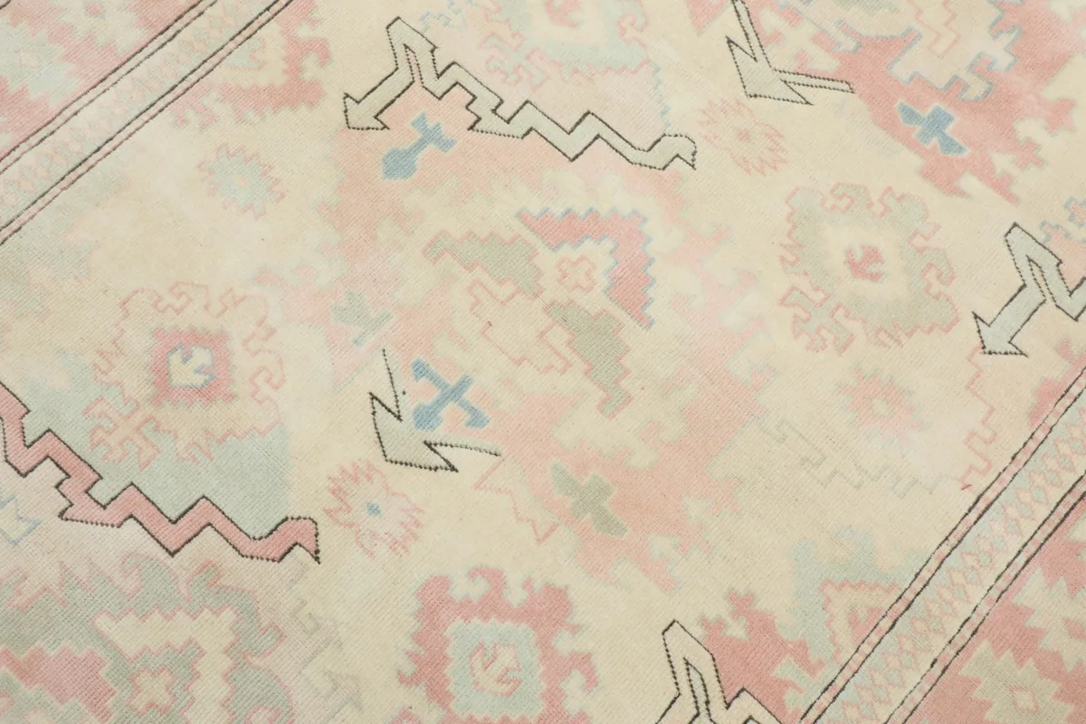 Detailed view of the rug's central motifs, featuring faded pink, blue, and gray geometric designs on a cream background.