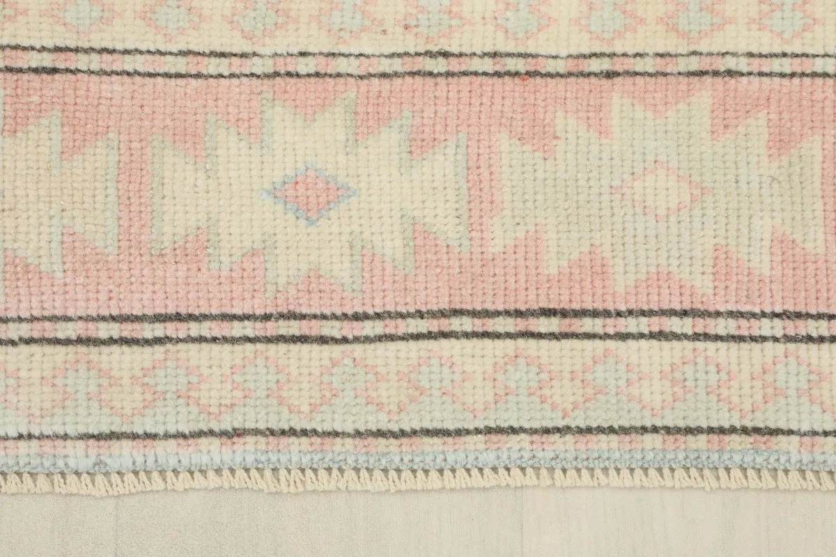 Close-up of the rug's border, displaying the repeating pink and cream tribal patterns and fine edge details.