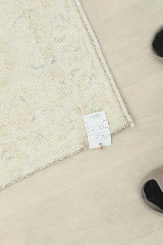 Overhead view of a corner of the rug with a size tag, next to feet for scale