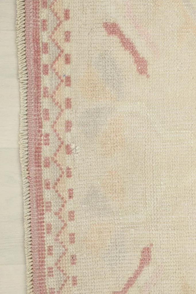 Detail of the rug's side border, showcasing the rose color and intricate geometric patterns