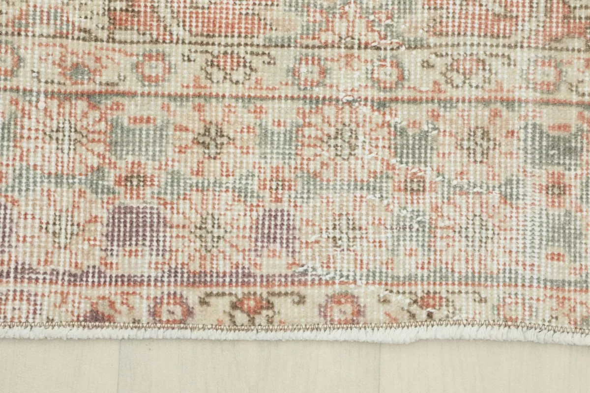 Detail of the rug's border design, featuring muted green, purple, and beige accents.