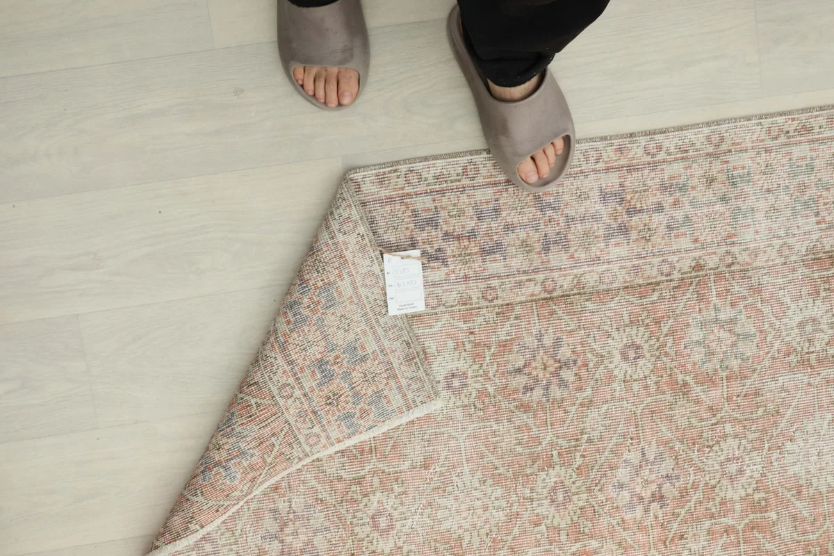 View of the rug's underside and tag, with feet for scale, showing the cotton foundation.