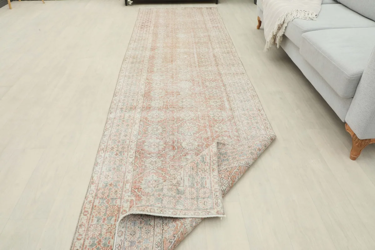 Runner rug partially unrolled in a room, displaying its full length and soft color palette.