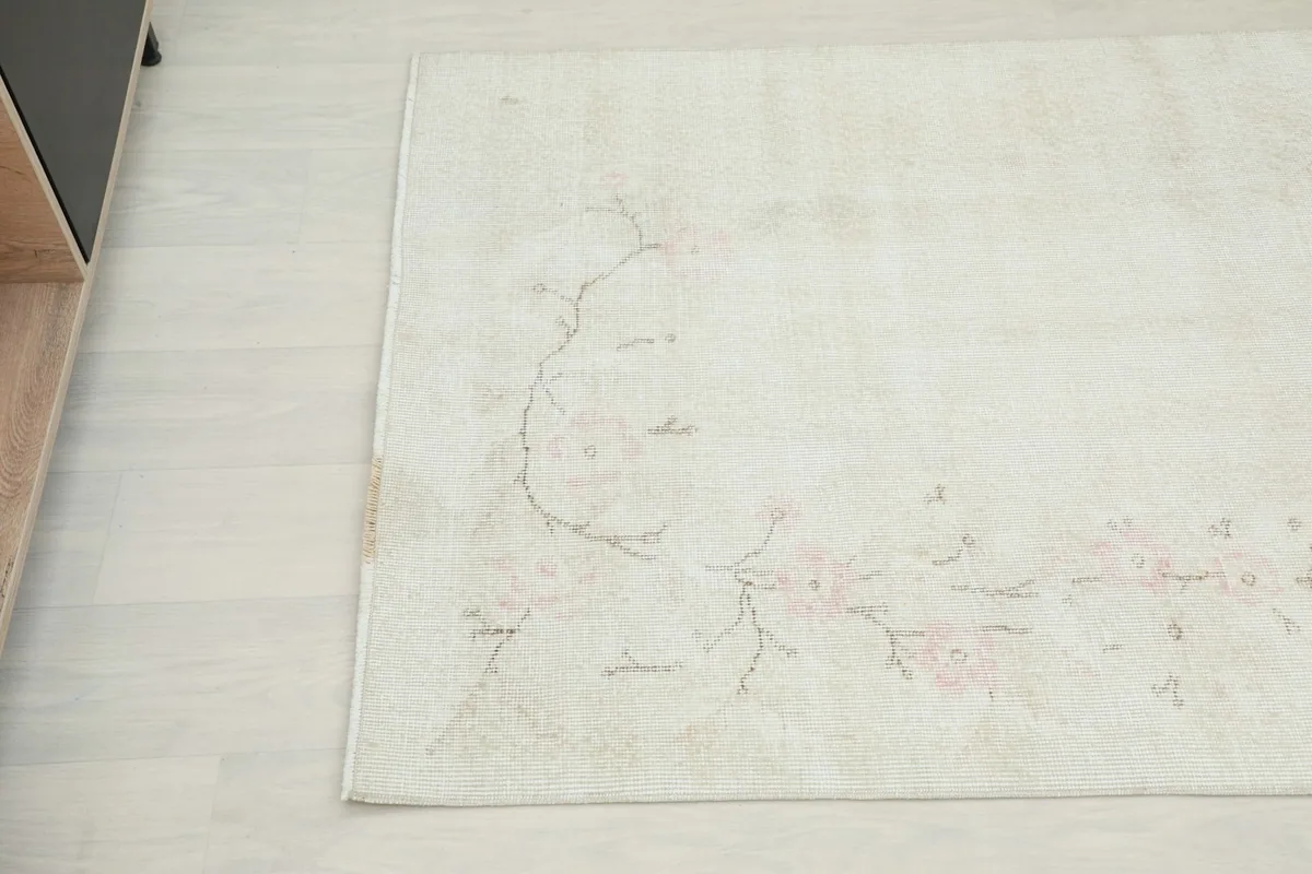 Corner detail showing the faded pink floral pattern and soft texture of the rug