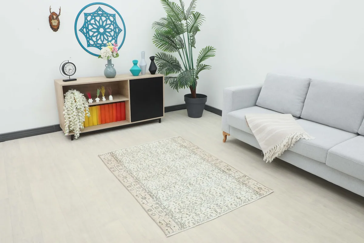 Vintage Anatolian rug with cream and olive tones displayed in a living room setting with a sofa and cabinet