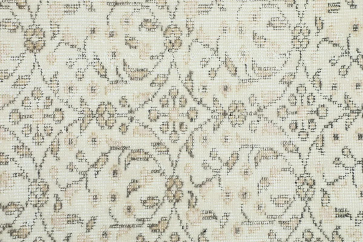 Detailed close-up of the hand-knotted floral and geometric patterns in olive and tan on a cream field