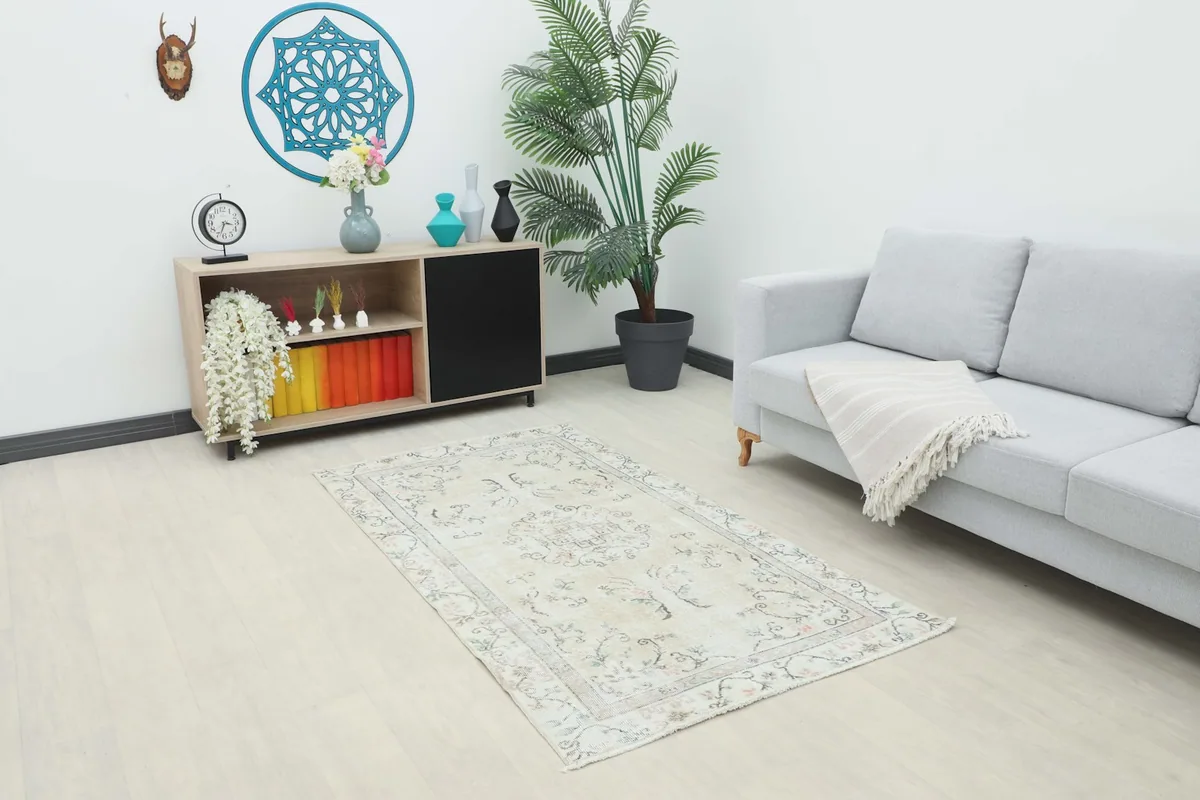 Vintage beige rug displayed in a living room setting with a sofa and cabinet.
