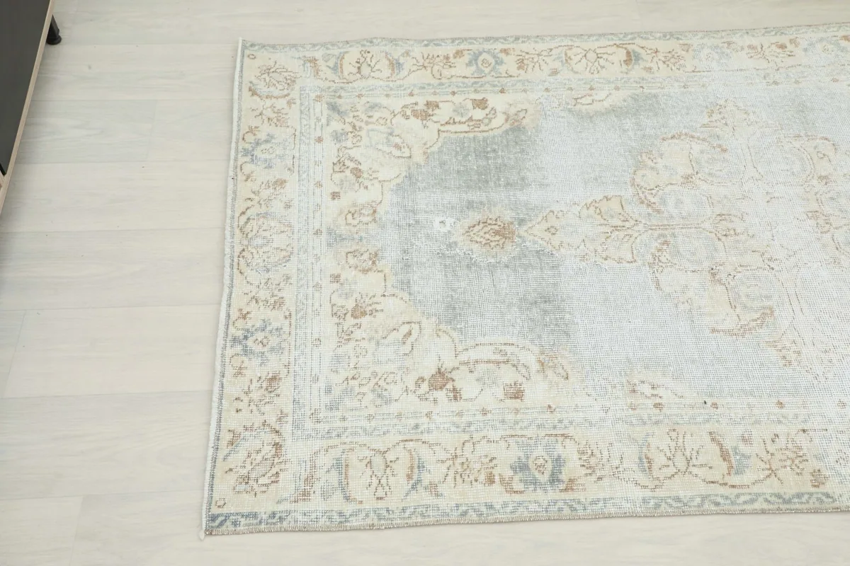 Close-up angled view of the lower left section of the blue vintage rug, revealing border details and color variations