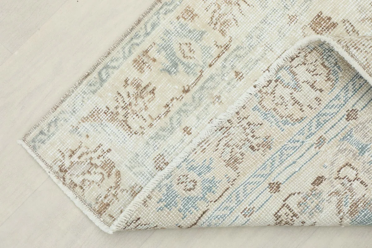 Corner of the rug folded back, showing the cotton foundation and the reverse side of the hand-knots