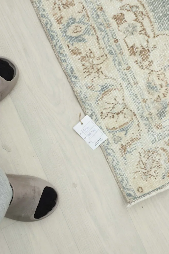 Overhead view of a corner of the rug with a tag, next to feet in slippers, showing scale and texture