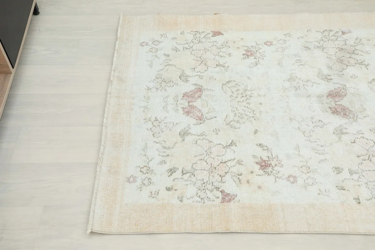 Detail view of the rug's border and a section of the cream field with subtle rose floral motifs.
