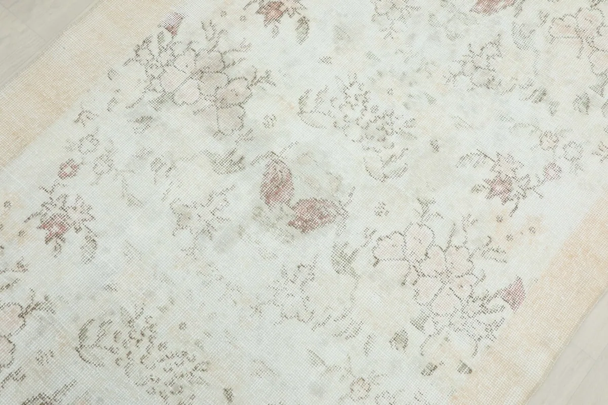 Close-up of the central floral patterns and gentle color variations on the vintage rug's cream field.