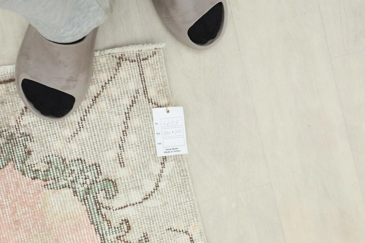 Corner of the rug with a size tag next to a person's feet for scale