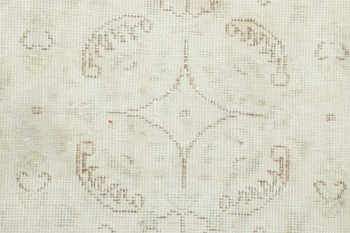 Detailed close-up of the hand-knotted wool pile and faded tan and green elements in the pattern