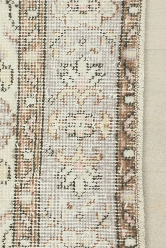 Detail of the rug's border, featuring a traditional pattern in beige and brown tones.