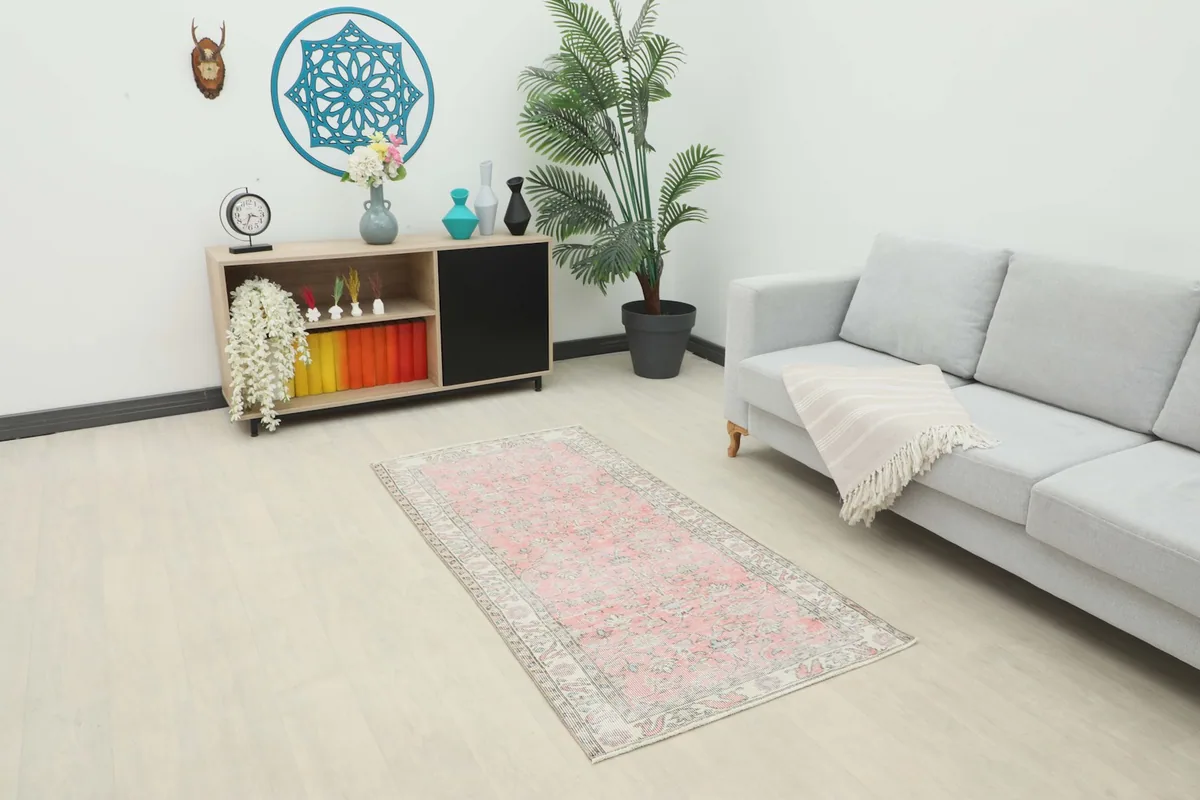 Vintage pink rug displayed in a modern room setting with a light gray sofa and wooden cabinet.
