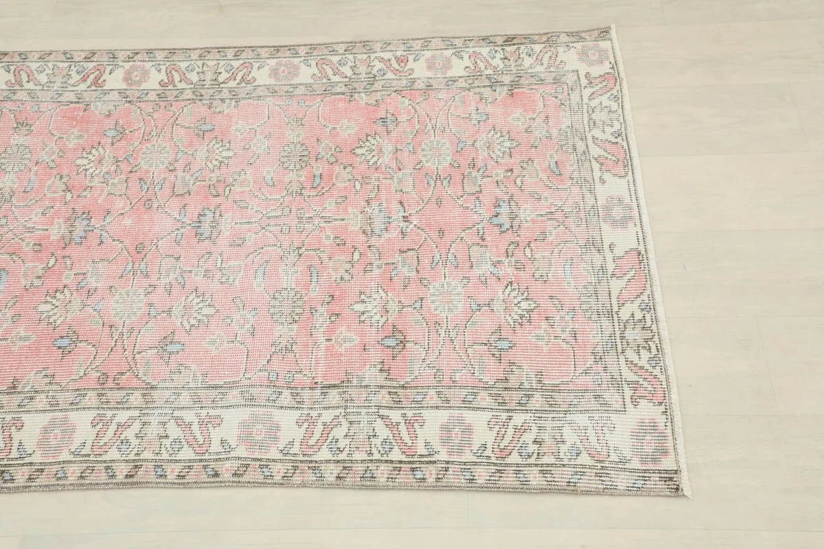 Close-up detail of the pink rug's border and main field with floral motifs and light wear.