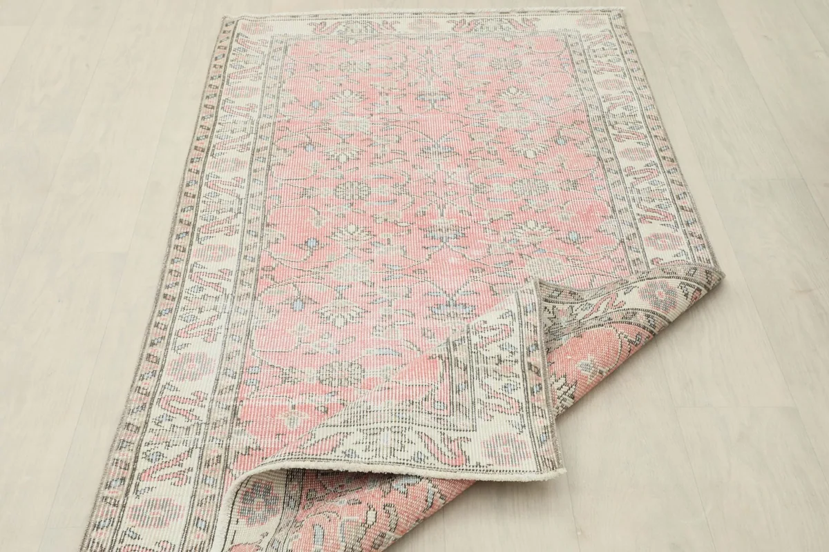 The pink vintage rug partially folded, illustrating its flexibility and construction.