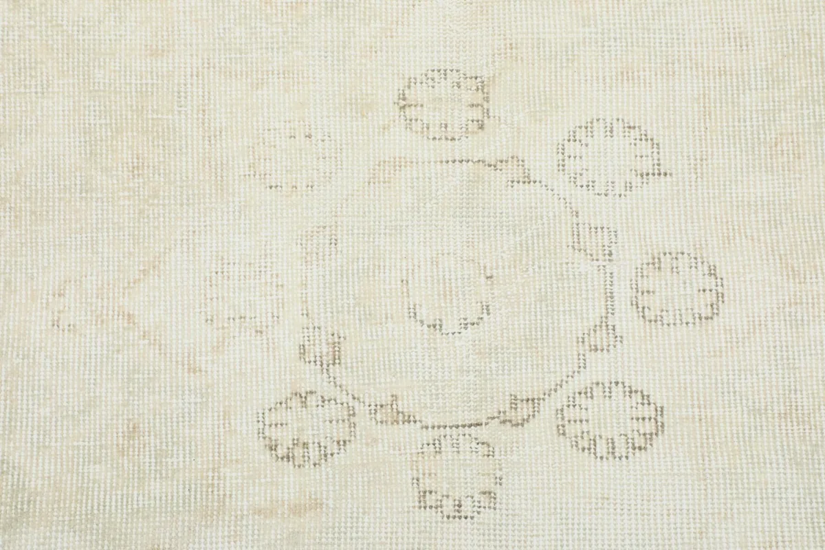 Close-up detail of the subtle floral motifs and distressed texture on the ivory wool pile