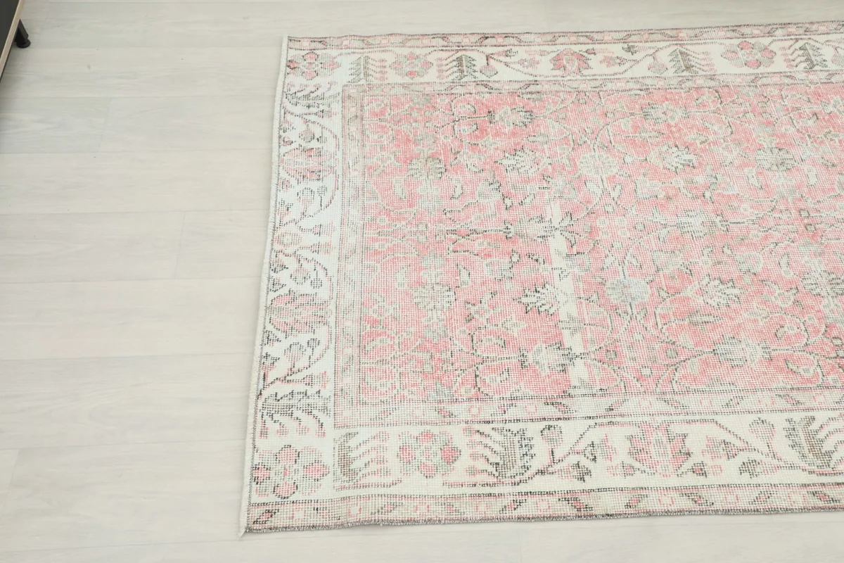 Close-up angled view of the top left corner of the vintage rug, showing the faded pink field.