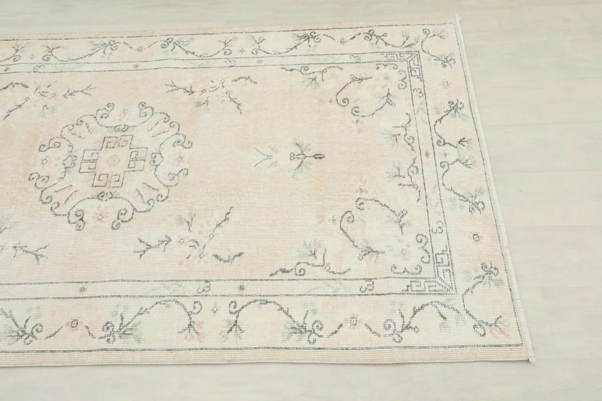 Close-up detail of the corner and border of the cream rug, highlighting the gray floral patterns.