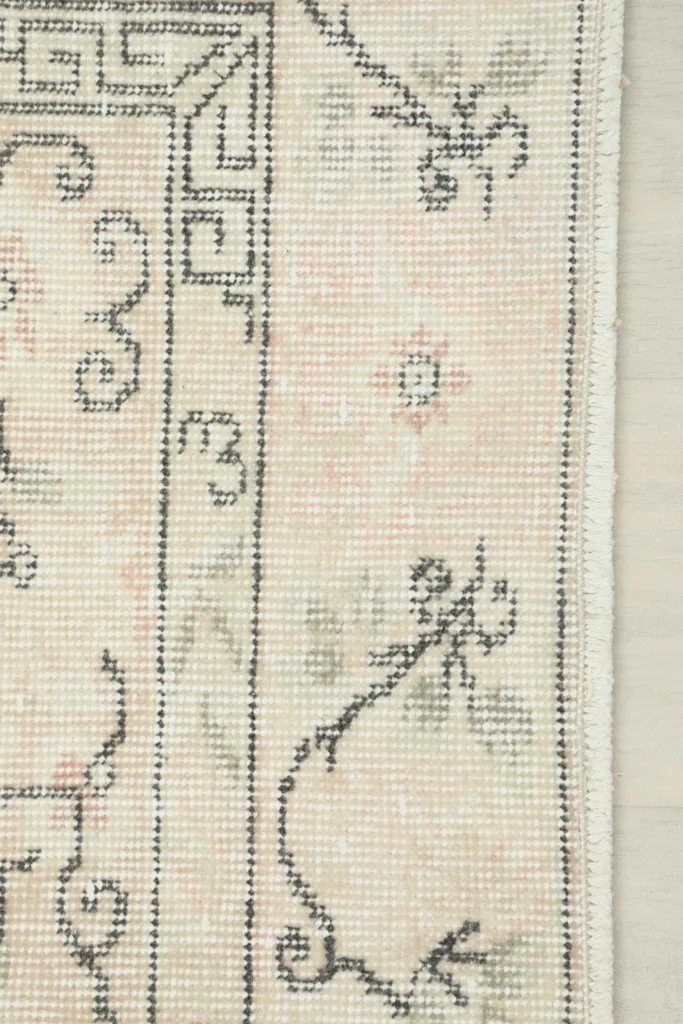 Detailed view of the rug's edge, showing the hand-knotted wool pile and the intricate gray and rose patterns.