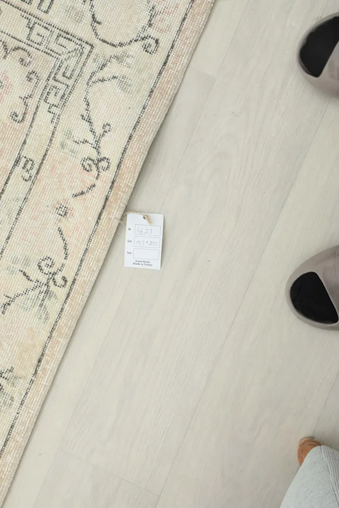 Top-down view showing the rug's label, indicating its origin and material, next to a pair of slippers.