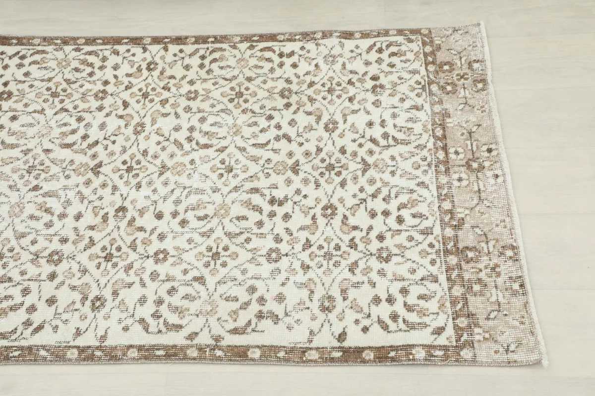 Close-up detail of the floral and geometric patterns in brown and tan on the ivory field