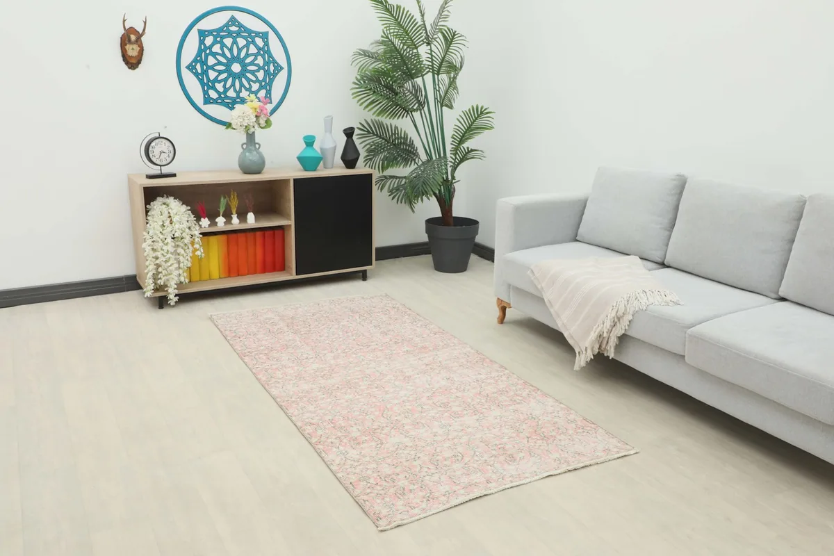 Vintage rose and gray rug placed in a modern living space with a sofa and cabinet, showing its scale.