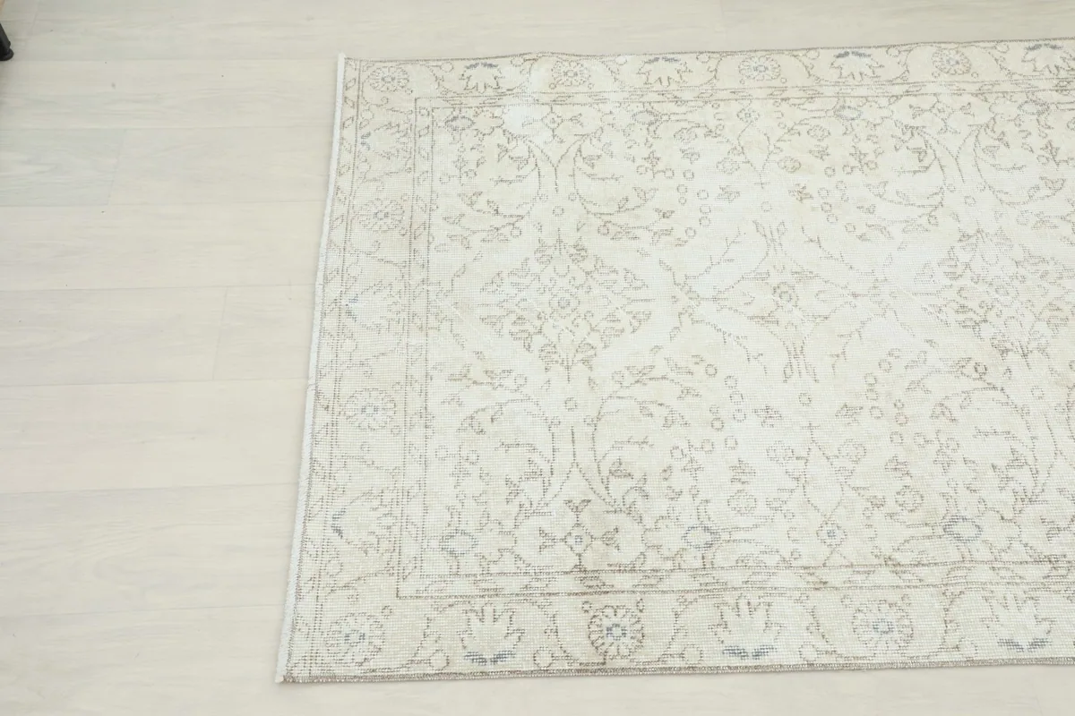 Close-up angled shot of the beige rug, emphasizing its muted tones and detailed border