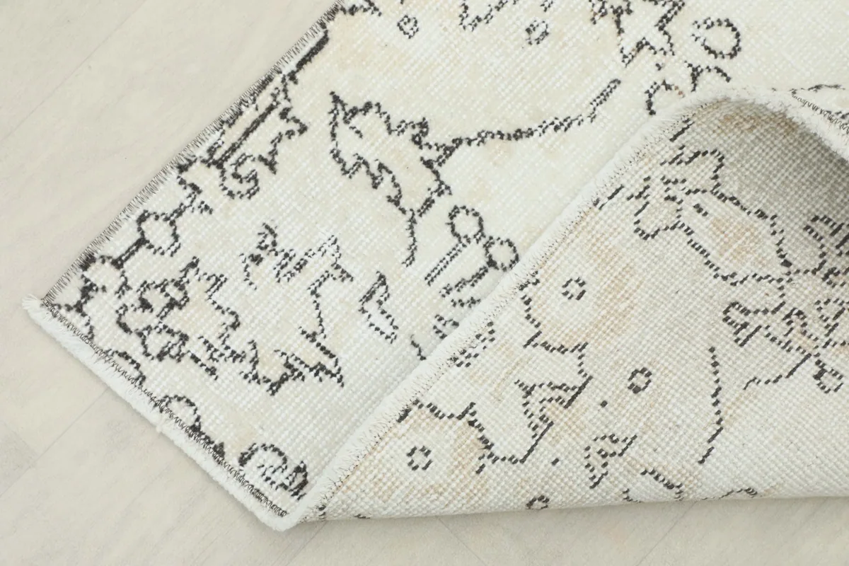 Corner of the rug folded back, showing the cotton foundation and the reverse side of the hand-knotted pile.