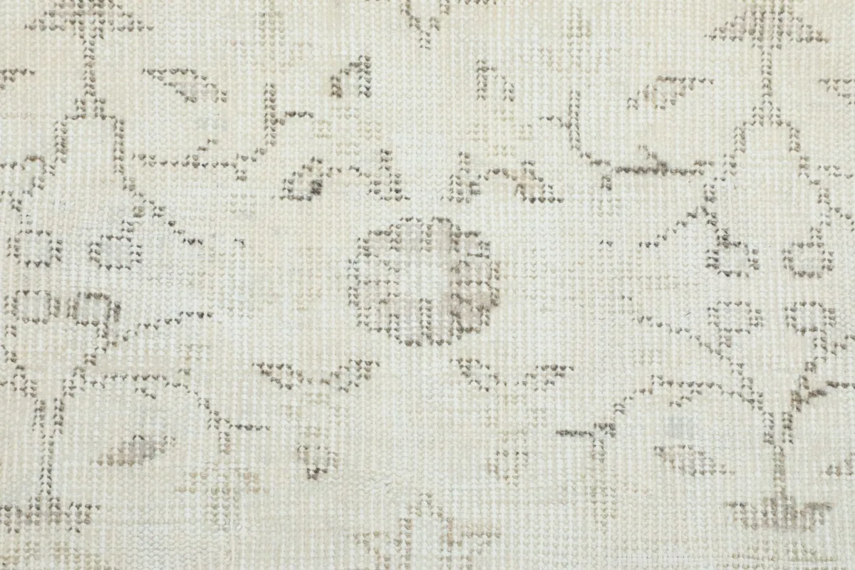 Extreme close-up of the hand-knotted texture and faded gray floral motifs on the ivory background
