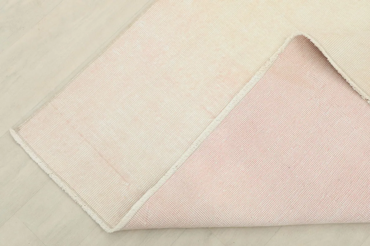 Corner of the rug folded back to show the cotton foundation and the reverse side with pinkish hue
