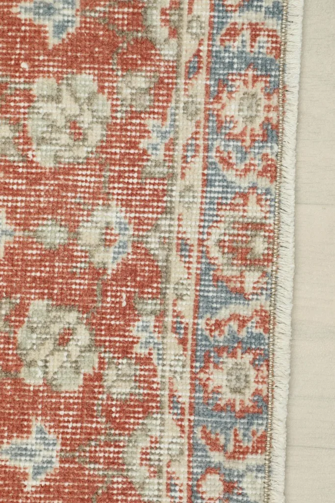 Close-up of the rug's border, displaying intricate blue and beige geometric patterns and fringe